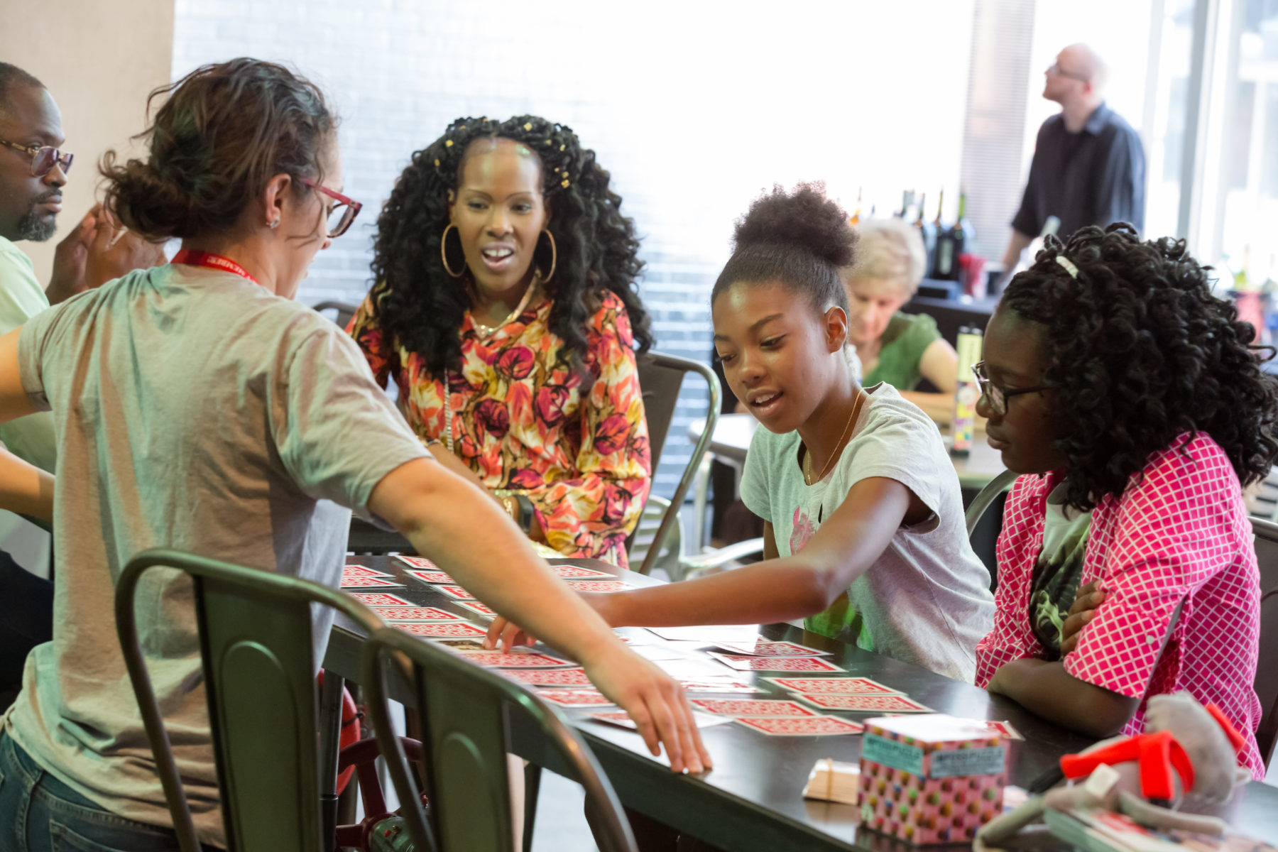 A group of people look at large cars spread out on a table in front of museum staff.