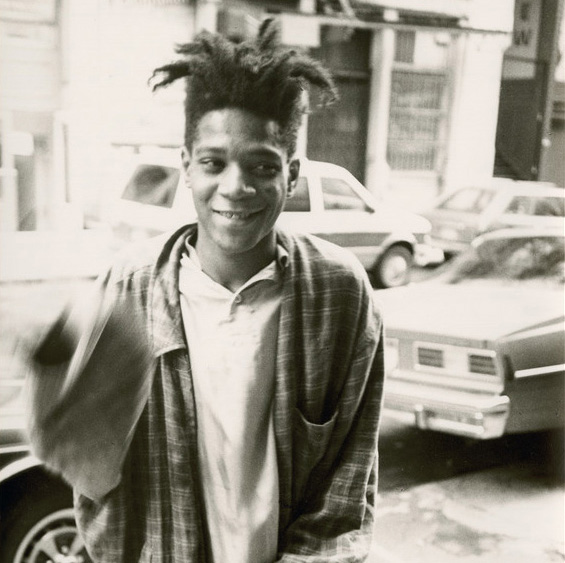Jean-Michel Basquiat stands smiling on a street in New York.