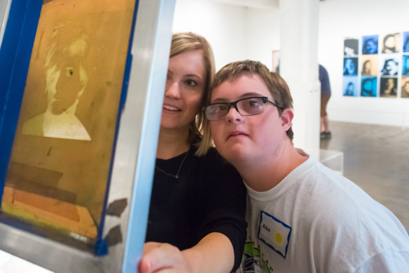 A teen and their parent in The Warhol galleries examine an exposed silkscreen featuring an image of Andy Warhol.