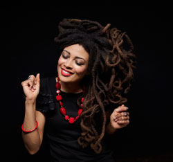 African American women smiles, eyes closed, with her head titled to the left, and her right hand is raised as if snapping her fingers.