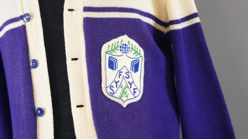 Close-up view of sweater, unbuttoned. The insignia includes two books, a globe, and ornamental wreaths.