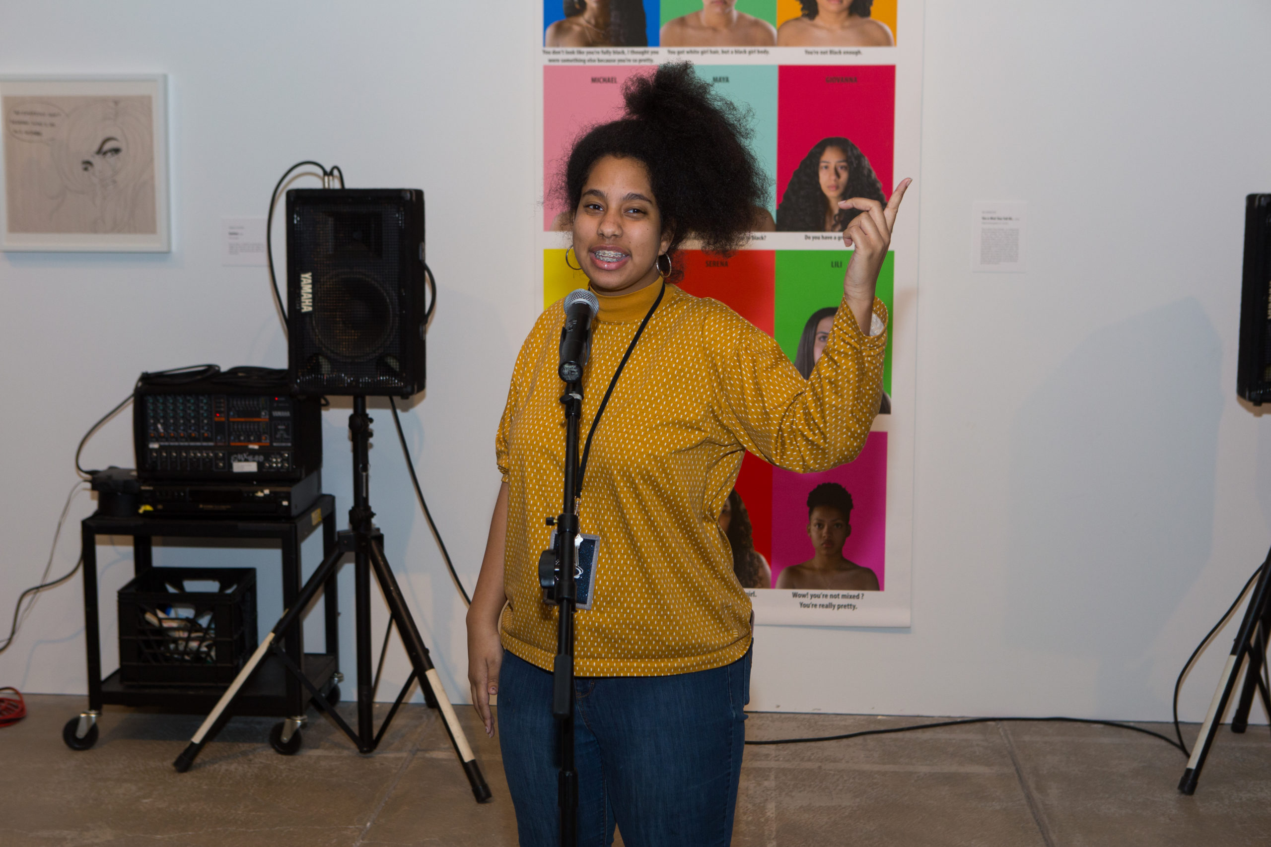 Young female performer, smiling as she points upwards and speaks in to microphone.