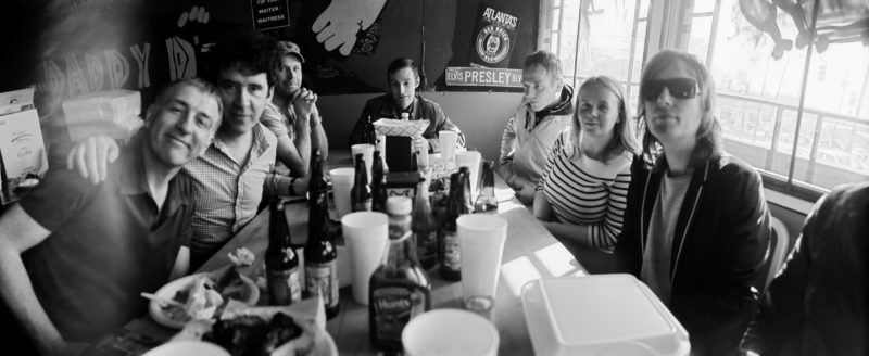 A black and white photo of a group of people sitting at a table in a restaurant looking at the camera.