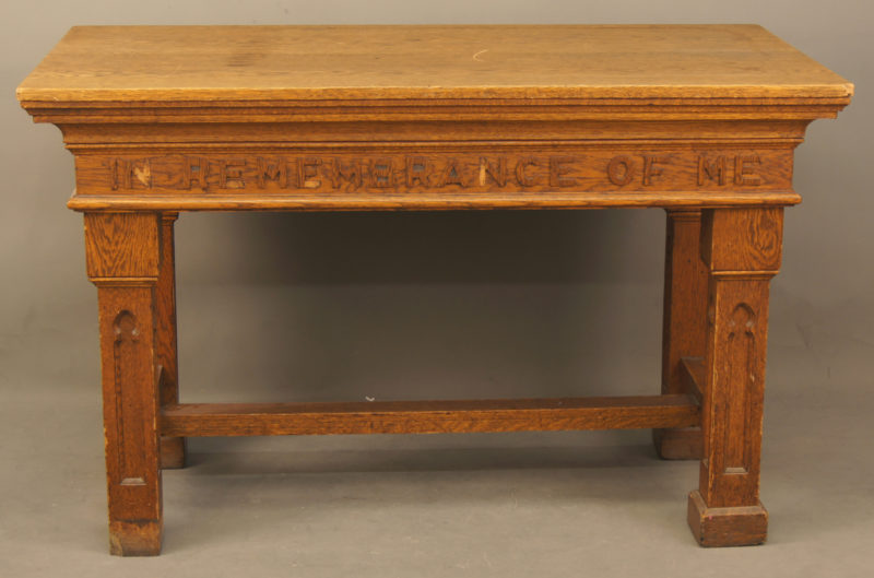 Front view of brown, wooden communion table. The table has “In Remembrance of Me” carved into its side.