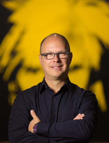 Photograph of Donald Warhola in front of a yellow and black Andy Warhol Self-Portrait