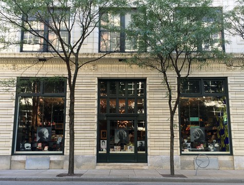 View of the face of a tan colored building with three large display windows. Art images can be seen on display through the windows.