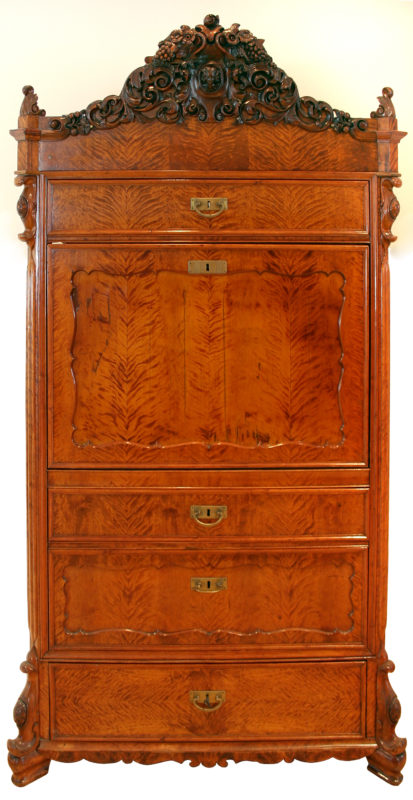 Front view of wooden heirloom desk. The desk is stained a light brown and has five visible closed compartments.