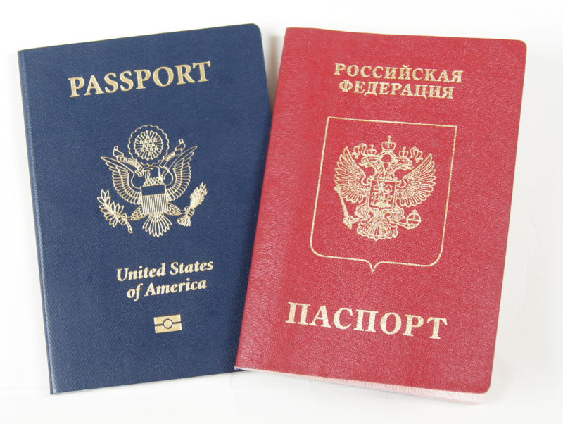 Front view of two passports. The passport on the left is a blue, American passport, while the passport on the right is a red, Russian passport