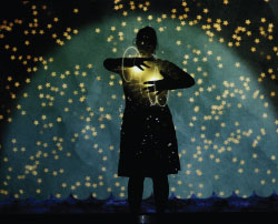 Silhouette of a person in front of a blue half-moon shape. Small yellow dots of light fill the image.