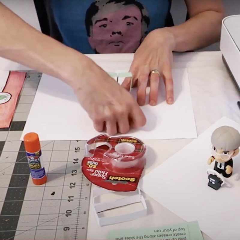 View of a woman's hands as she works with paper, glue, tape, and scissors.