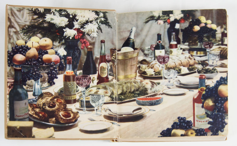 View of cookbook open to the first pages of its interior. The pages depict a realistic spread of fine food and beverages.