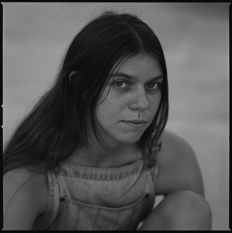 Black and white photograph of a person with long, straight, dark hair looking towards the camera.