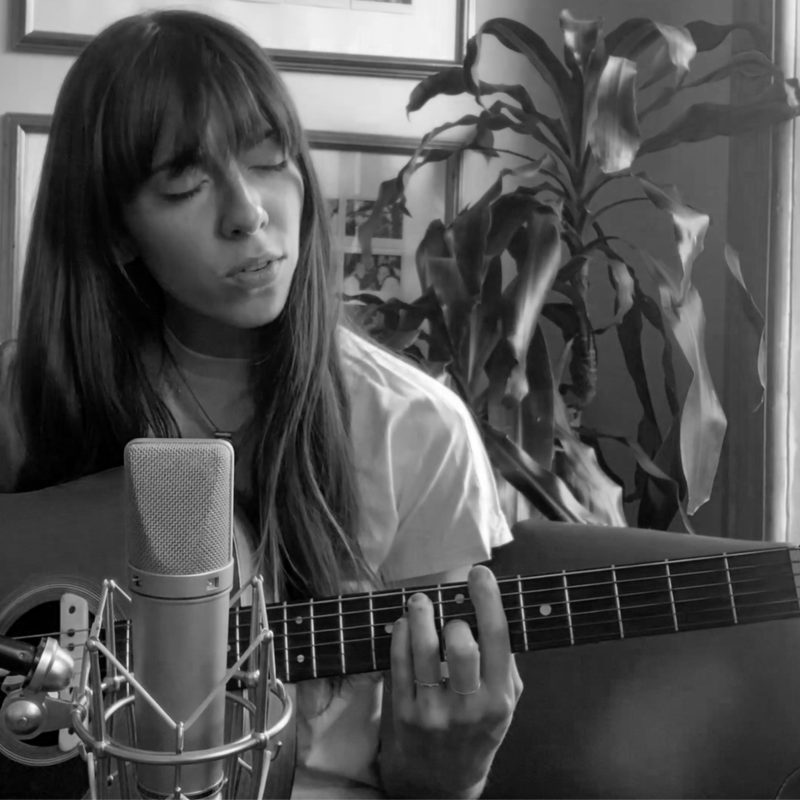 Woman plays guitar while sitting in front of a microphone