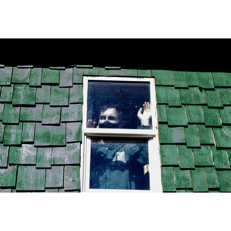 Photo of a person wearing a mask, looking out of the window