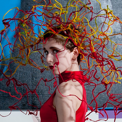 A side view of a person wearing a red sleeveless top with a yellow and red avant-garde headdress.